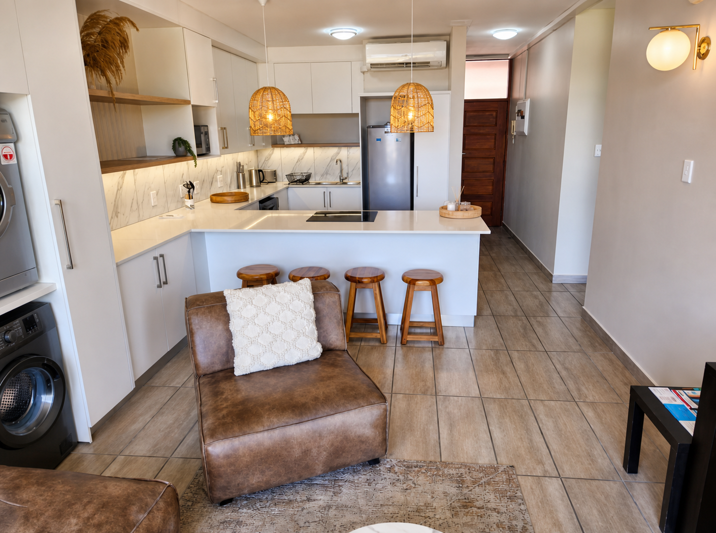 The white kitchen with marble splashback, induction hob, rattan pendants and four wooden bar stools