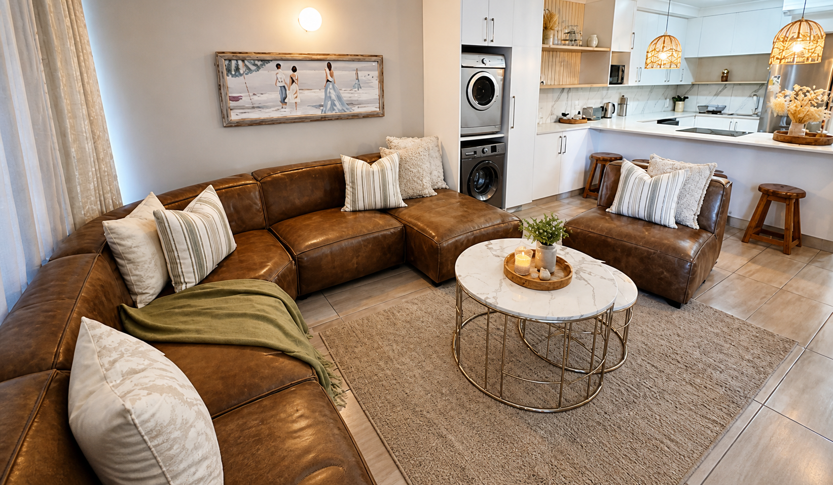 The open-plan lounge and white kitchen at Pebbles, leather corner suite and marble coffee table with rattan pendants over the peninsula