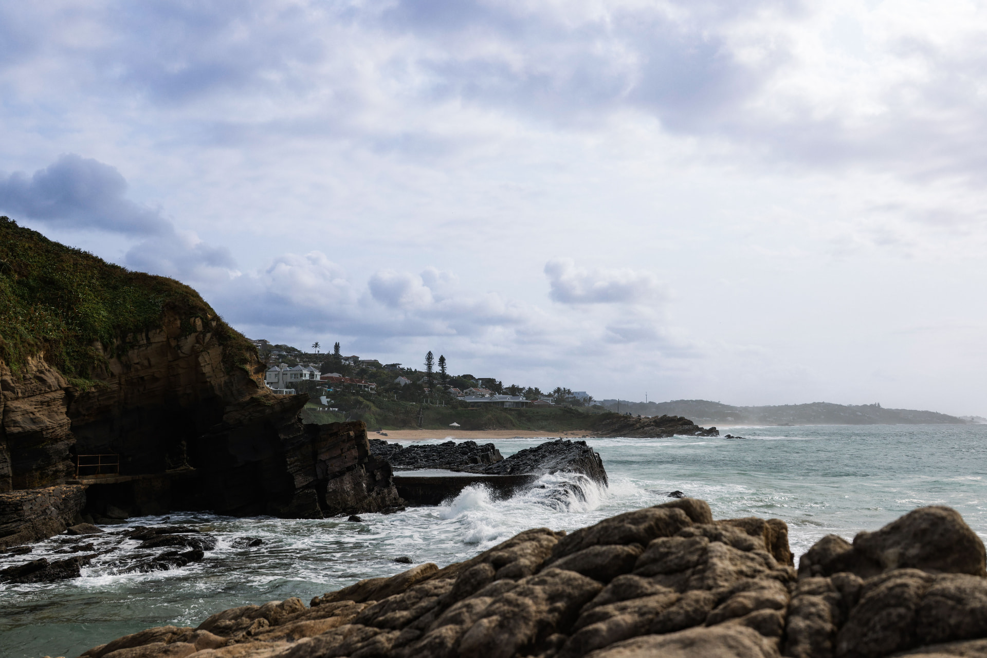 A rocky cove below sandstone cliffs, with clifftop houses along the coast beyond